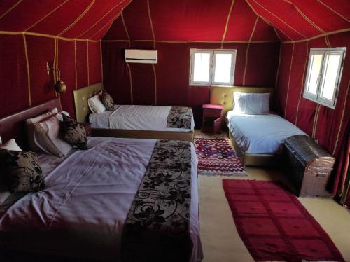 a room with three beds in a room with red walls at Merzouga Desert Experience Camp-Erg Chebbi Sunset & Camel Ride in Merzouga