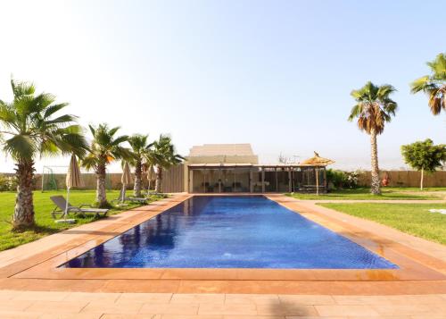 a swimming pool with palm trees in front of a building at Peaceful Family Villa on a Farm with Private Pool and Stunning Mountain Views in Agadir