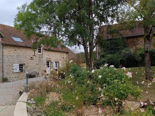 - un jardin en face d'un bâtiment en pierre orné de fleurs dans l'établissement Charmant gîte en Normandie avec jardin et activités à sensations - FR-1-410-300, à Arçonnay