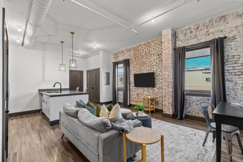 a living room with a gray couch and a brick wall at Brick & Bed Riverfront Lofts, PC 203 in Saint Louis