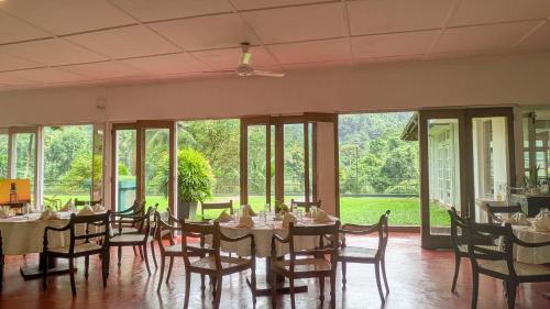 a dining room with tables and chairs and large windows at Heritage Kithulgala Rest House - Historic Home to a Bird Sanctuary in Kitulgala