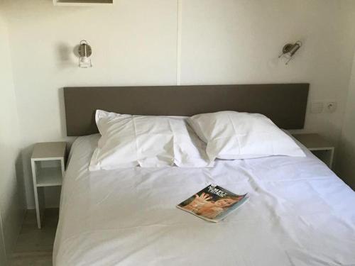 a bedroom with a white bed with a book on it at Mobil-home pour 6 avec terrasse à Avrillé - API-1-52-728 in Avrillé