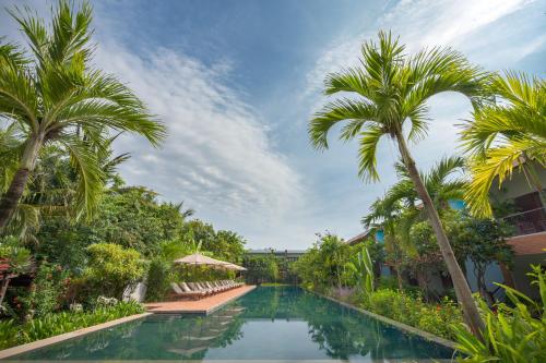a resort pool with palm trees and chairs at Khmer House Resort in Siem Reap