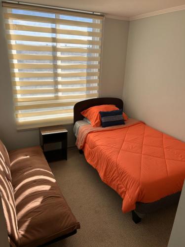 a bedroom with a bed with an orange comforter and a window at Condominio nuevo lantaño in Chillán