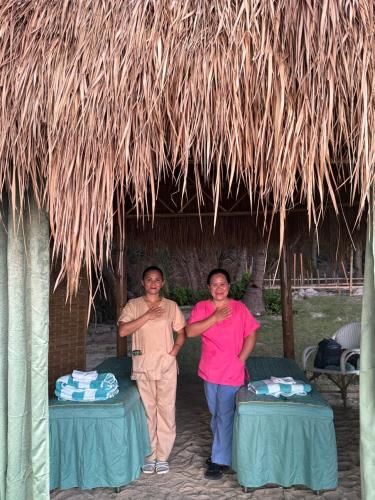 a man and woman standing under a straw hut at The Beach House Ocam Ocam in Busuanga