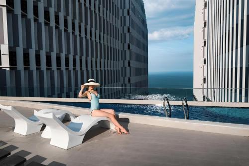 a woman sitting on a bench next to a pool at Apec Mandala de Suite Mũi Né in Mui Ne