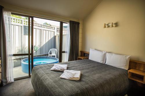 a bedroom with a bed and a balcony with a tub at Bennetts Thermal Motor Inn in Tauranga
