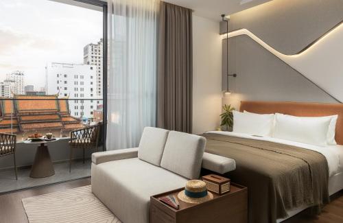 a hotel room with a bed and a chair and a window at Bassac Signature Hotel & Residence in Phnom Penh