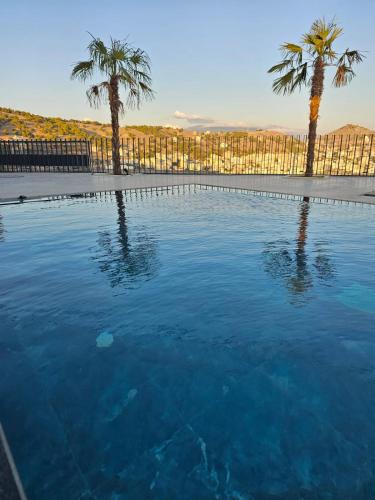 a swimming pool with palm trees and a fence at Hotel Selavi in Sarandë