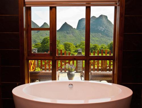 a bath tub in front of a window with a view at Yangshuo Coco Garden Hotel in Yangshuo