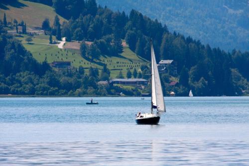 a sailboat on a large lake with a small boat at Haus Lackner am Weissensee in Kärnten in Weissensee