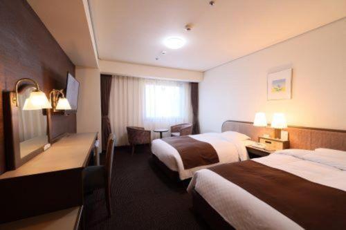 a hotel room with two beds and a desk at Sunroute Aomori Hotel in Aomori