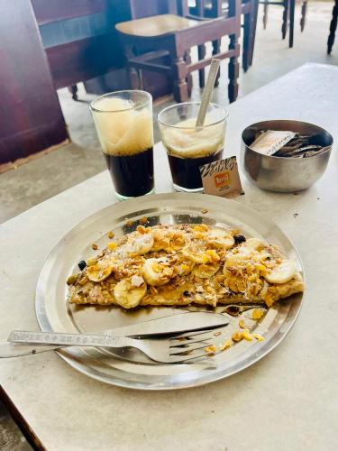 a pizza on a plate with a fork and two drinks at Hotel White House - A Family Homestay in Pushkar