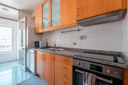 a kitchen with wooden cabinets and a sink at OceanSide - EcoHost - Apartamento para 4 pessoas em frente à praia a 200m do Metro do Porto in Matosinhos