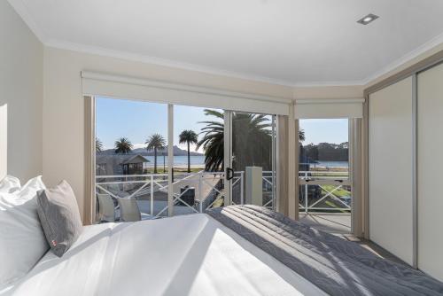 a white bedroom with a bed and a balcony at Crow's Nest Apartments in Whitianga