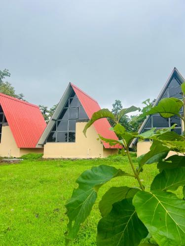 a building with a red roof on a green field at Huts And Hunters Resort Saputara in Saputara