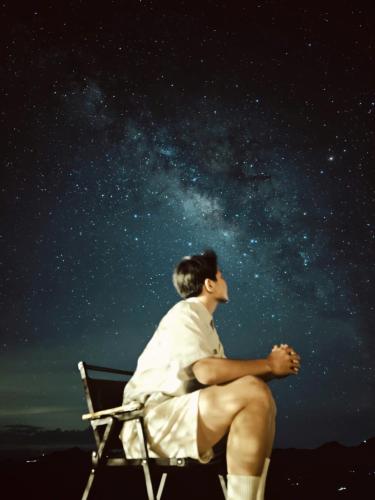a man sitting in a chair looking up at the stars at Nơi Ấy Homestay in Bắc Yên