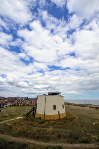 a building in the middle of a field near the ocean at Martello Sunrise - Luxury 3-bedroom Seaview Beach House in Felixstowe