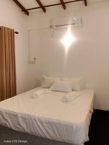 a bed with white sheets and a light on the wall at Cozy Conner Villa in Weligama