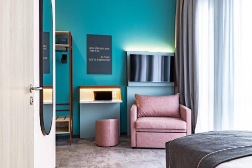 a bedroom with a pink chair and a blue wall at Holiday Inn - the niu, Pax Berlin Airport by IHG in Berlin