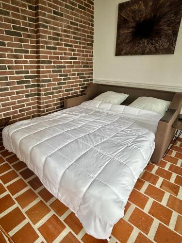 Cette chambre comprend un grand lit blanc et un mur en briques. dans l'établissement Logement entier studio vue mer, à Villers-sur-Mer