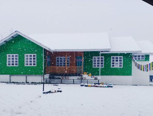 a green building with snow in front of it at Odyssey Stays Mechuka in Bāsār
