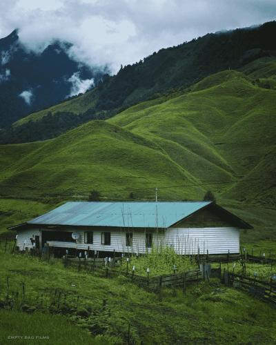 a white house with a blue roof in a field at Odyssey Stays Mechuka in Bāsār