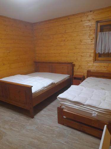 two beds in a room with wooden walls at Barangoló vendégház in Bárdudvarnok