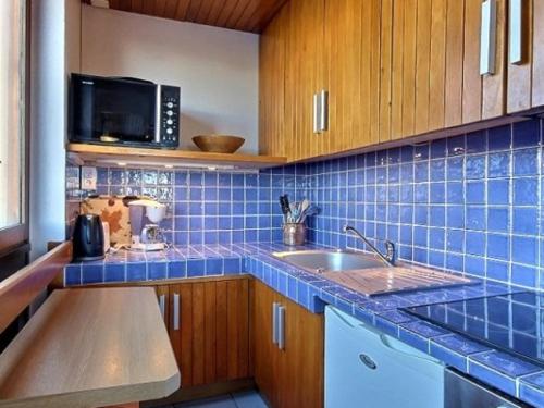 Il comprend une cuisine dotée de carrelage bleu, d'un évier et d'un four micro-ondes. dans l'établissement Appartement cosy au pied des pistes avec balcon et équipements modernes - FR-1-455-61, à La Plagne