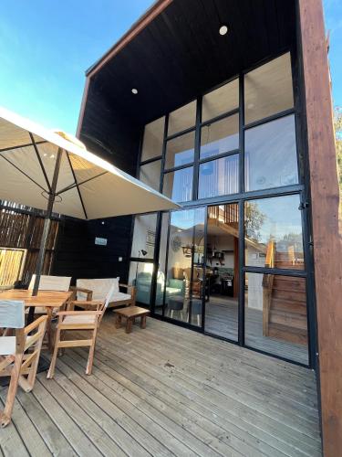 a house with a deck with a table and an umbrella at Lodge KARKÚ in Pichilemu