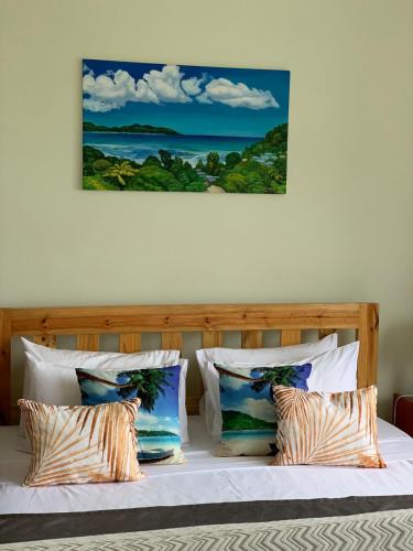 a bed with pillows and a painting on the wall at Sunset View Self Catering in Anse Boileau