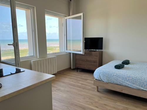 a bedroom with a bed and a television and windows at Bleu Langrune - Studio vue Mer in Langrune-sur-Mer