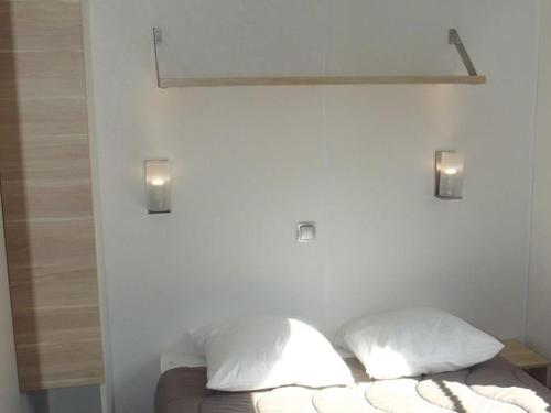 ein Bett mit zwei Kissen und zwei Lichtern an der Wand in der Unterkunft Mobil home confortable avec terrasse - API-1-52-217 in Le Grand Serre