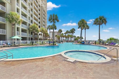 a swimming pool with palm trees and a building at Grand Panama by Panhandle Getaways in Panama City Beach