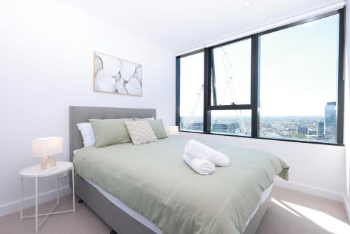 a white bedroom with a bed with a large window at 14D Abnb-Style Elegant CBD Sanctuary with Balcony, Pool and Skyline Views in Melbourne