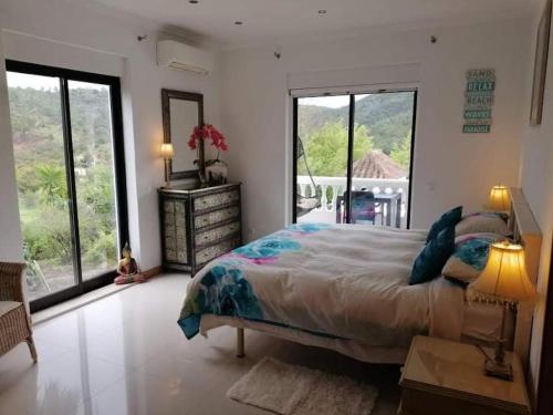 a bedroom with a large bed and large windows at casa do lago in Monchique