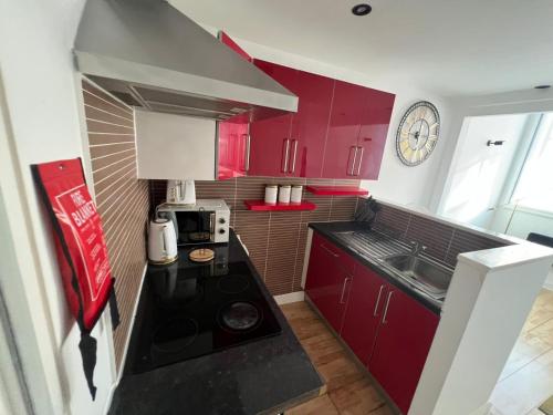 a small kitchen with red cabinets and a clock on the wall at Stylish Cozy 5-Apartments - Birmingham Central in Birmingham