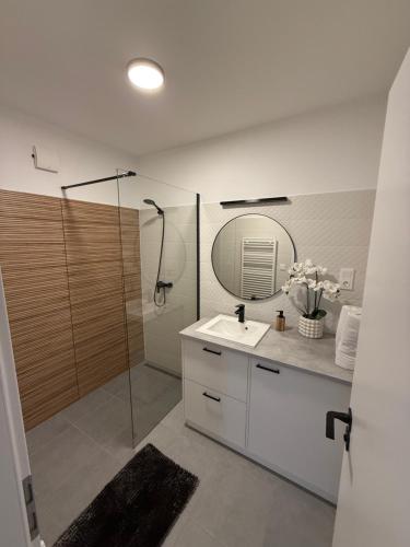 a bathroom with a sink and a shower with a mirror at Dream Premium Apartman in Mosonmagyaróvár