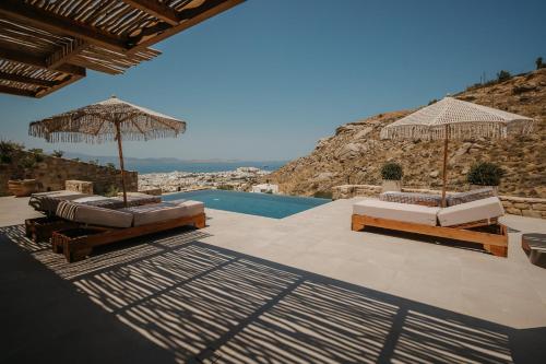 a patio with two beds and umbrellas and a pool at GkF Luxury Villas in Naxos Chora