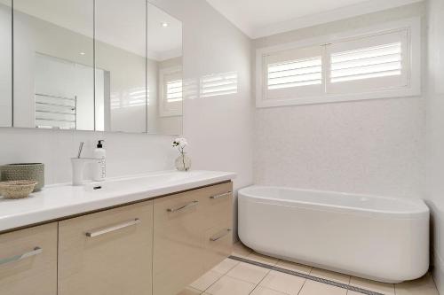 a white bathroom with a tub and a sink at Drift - Ocean & Panoramic Views At Coledale in Coledale