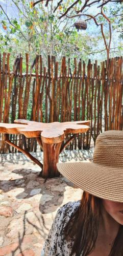 a woman wearing a hat sitting next to a wooden table at Cabañas Aldea Yalcón in Valladolid