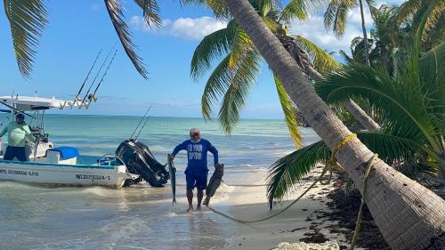 a man standing on the beach next to a boat at Casa Paraiso Punta Allen in Punta Allen