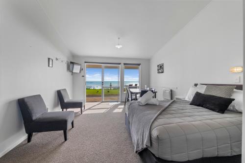 a bedroom with a bed and a chair and a balcony at Belt Road Seaside Holiday Park in New Plymouth