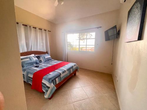 a bedroom with a bed with a red blanket and a window at Villa Española in Sosúa