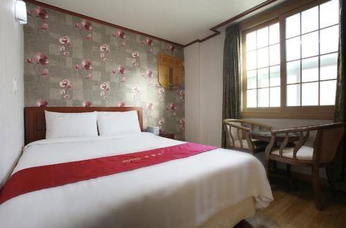 a bedroom with a bed and a table and window at Orange Hotel Jeju in Jeju