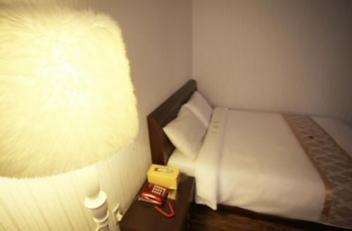 a small room with a bed and a lamp at Orange Hotel Jeju in Jeju