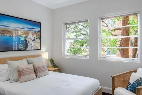 a white bedroom with a bed and two windows at Heatherbrae II - Stunning Harbour Bridge Views! in Sydney