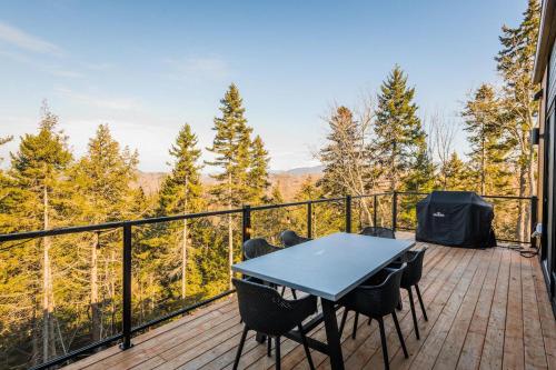 a table and chairs on a deck with a view of trees at Chalet Xo Tremblant - 5brs, Private Baths, Spa, Sauna & Rooftop in La Conception