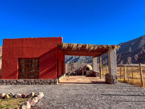 un edificio rosso con un tetto e montagne sullo sfondo di Wayra del Cerro a Purmamarca