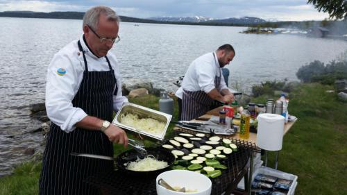 two men cooking food on a grill next to the water at Rondane Høyfjellshotell in Mysusæter